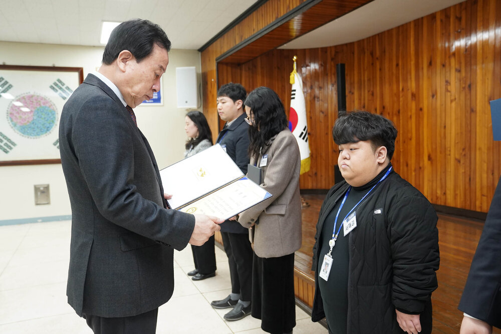 3월 정례조회에서 정장을 입은 남성이 검정 패딩을 입은 남성에게 표창장을 전달하는 모습