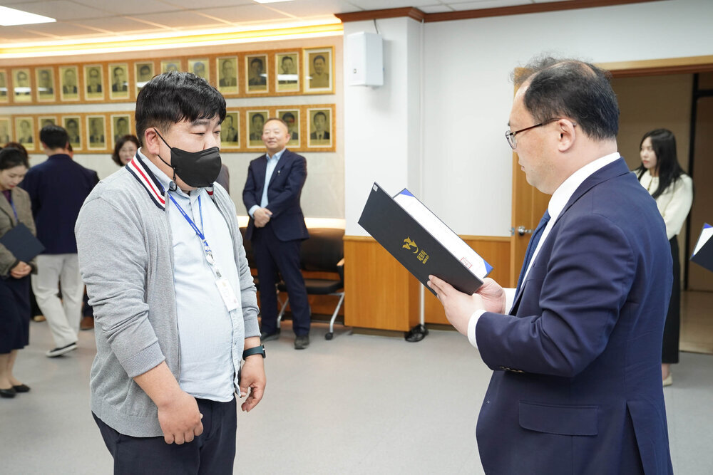 수시인사 임용장 수여식에서 정장을 입은 남성이 회색 점퍼를 입고 마스크를 착용한 남성 직원에게 임용장을 전달하는 모습