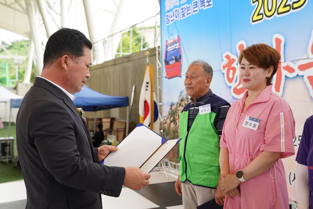 곤색 정장을 입고 안경을 낀 남성이 연분홍 트레이닝 수트를 입은 전수정에게 상장을 수여하고 있다
