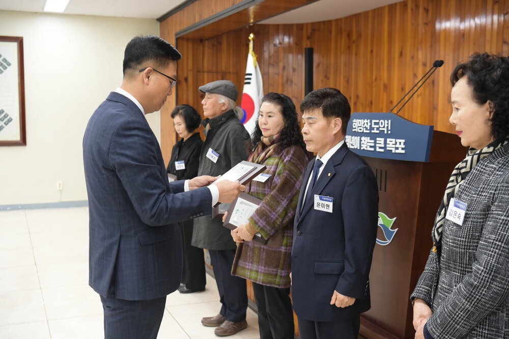 3월 정례조회에 정장을 입고 안경을 낀 남성이 짙은 네이비색 위아래 정장을 입은 윤미현에게 패를 수여하고 있다.